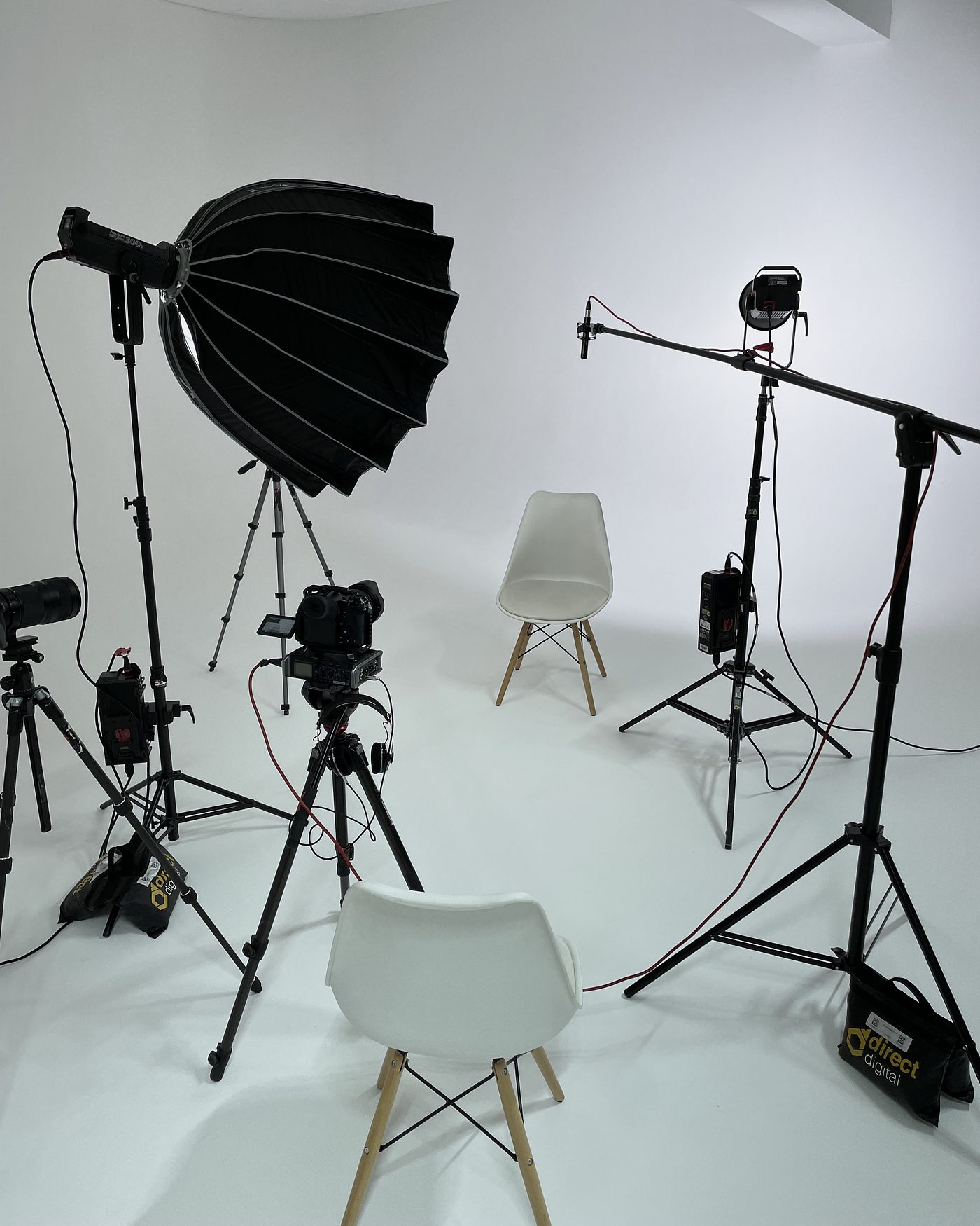 Two-camera interview set in a white studio with softbox, boom microphone and two chairs